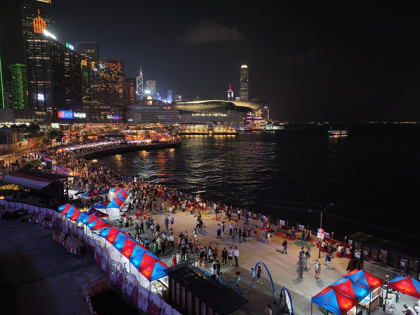 Aerial view of Waterfront Carnival's red-and-blue tent-lined promenade against the Hong Kong skyline at night